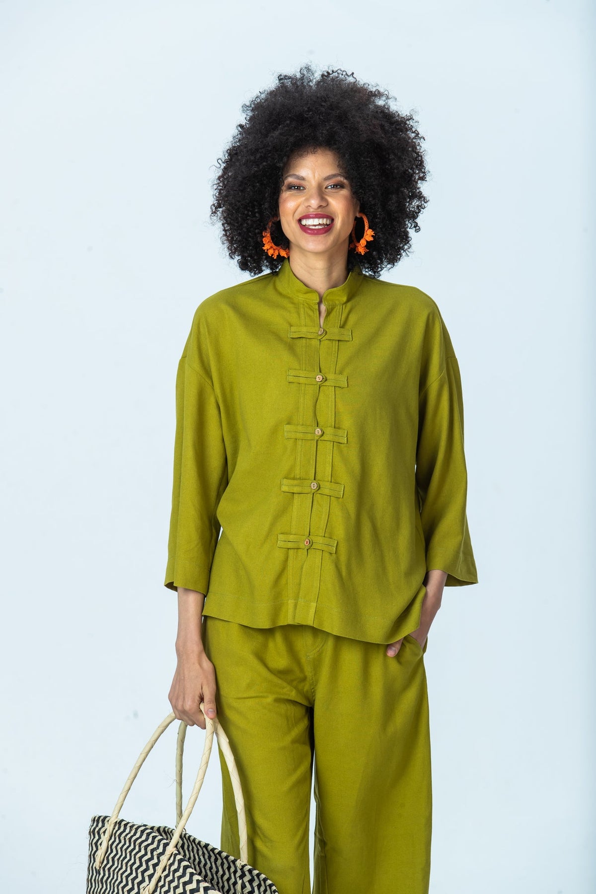Kinsley chartreuse kaftan-style shirt, front view with hand in pocket, holding a woven basket