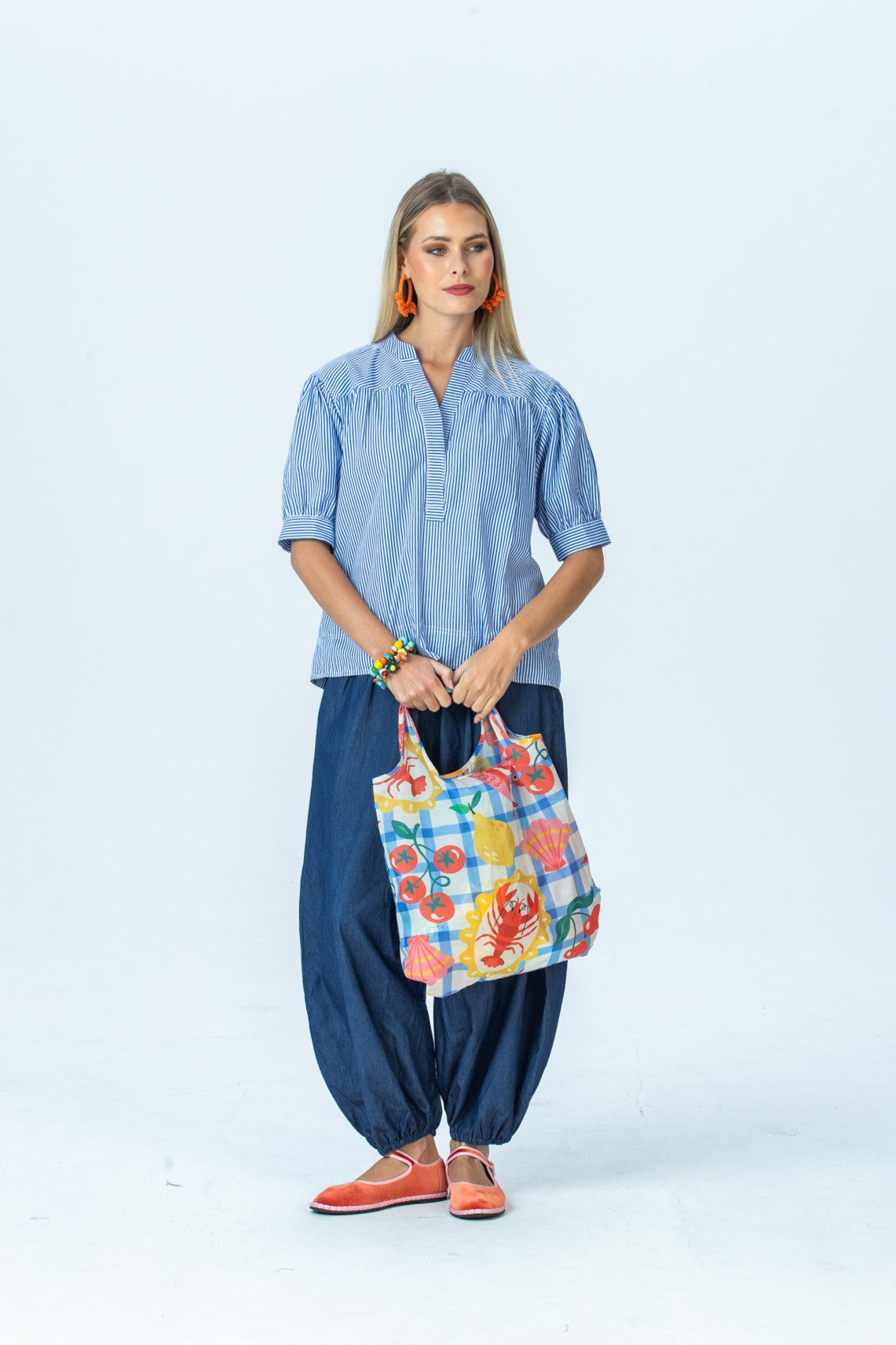 Tatum blue stripe shirt, front view full length holding a tote, looking to the side