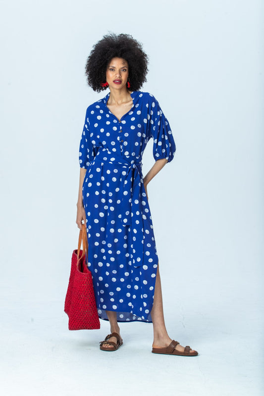 Sloane royal blue polka dot dress, front view full length, belted, holding a red woven tote