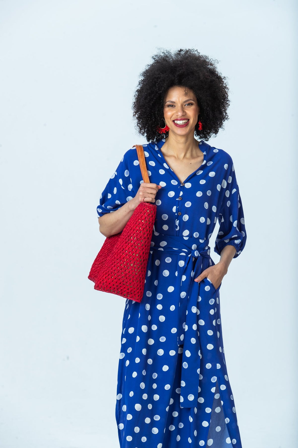 Sloane royal blue polka dot dress, front view with a red tote on the shoulder, hand in pocket