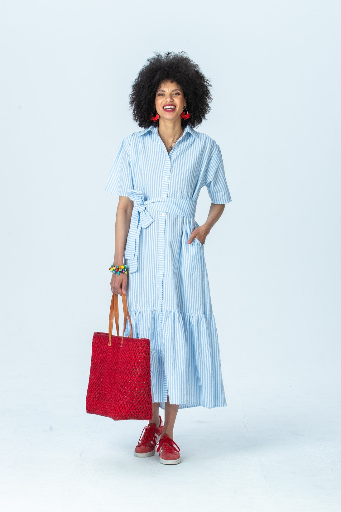 Frankie blue stripe shirt dress, front view full length, belted, holding a red woven tote