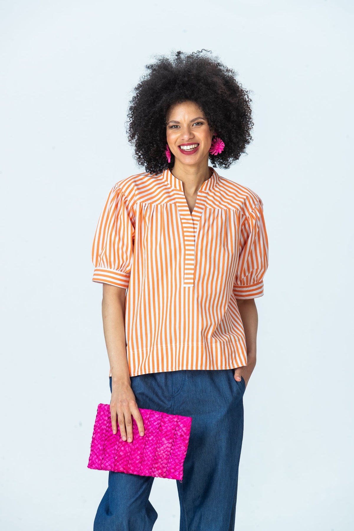 Tatum orange stripe shirt, front view holding a pink woven clutch, hand in pocket
