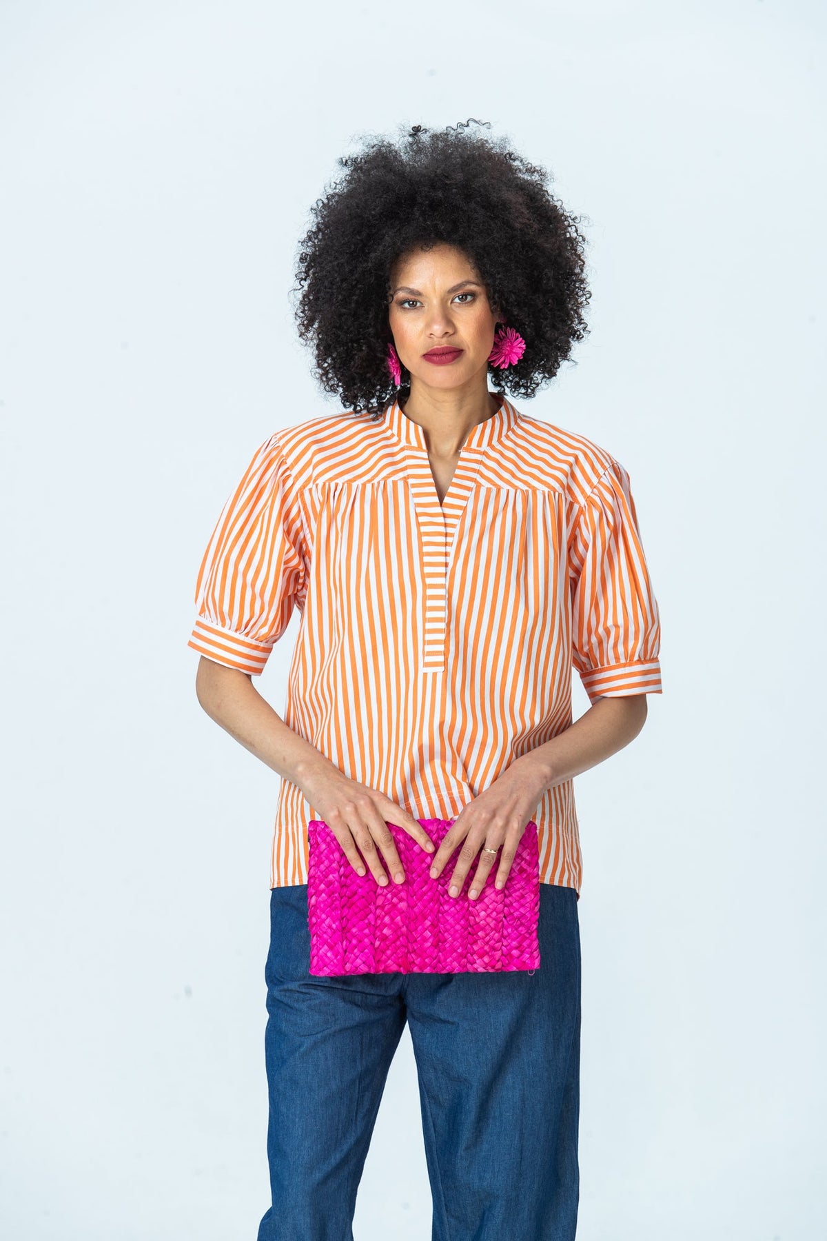 Tatum orange stripe shirt, front view holding a pink clutch with both hands