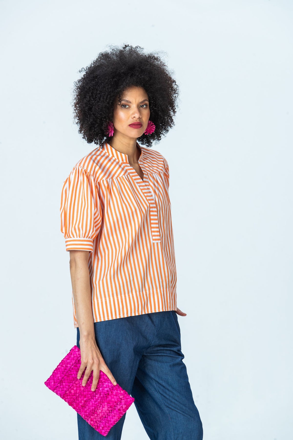 Tatum orange stripe shirt, three-quarter view holding a pink clutch