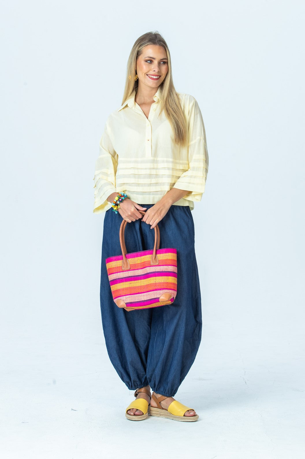 Serafina pale yellow shirt, front view full length holding a woven tote with both hands