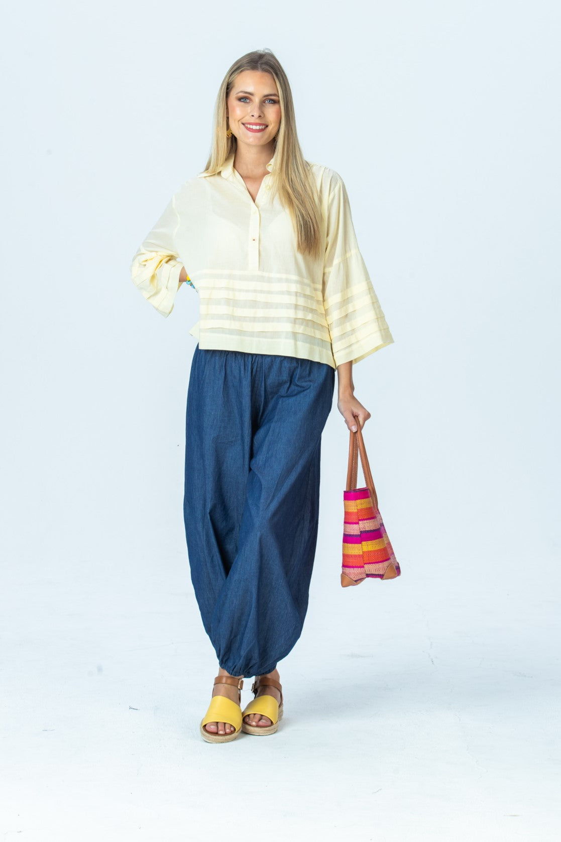 Serafina pale yellow shirt, front view full length holding a woven tote