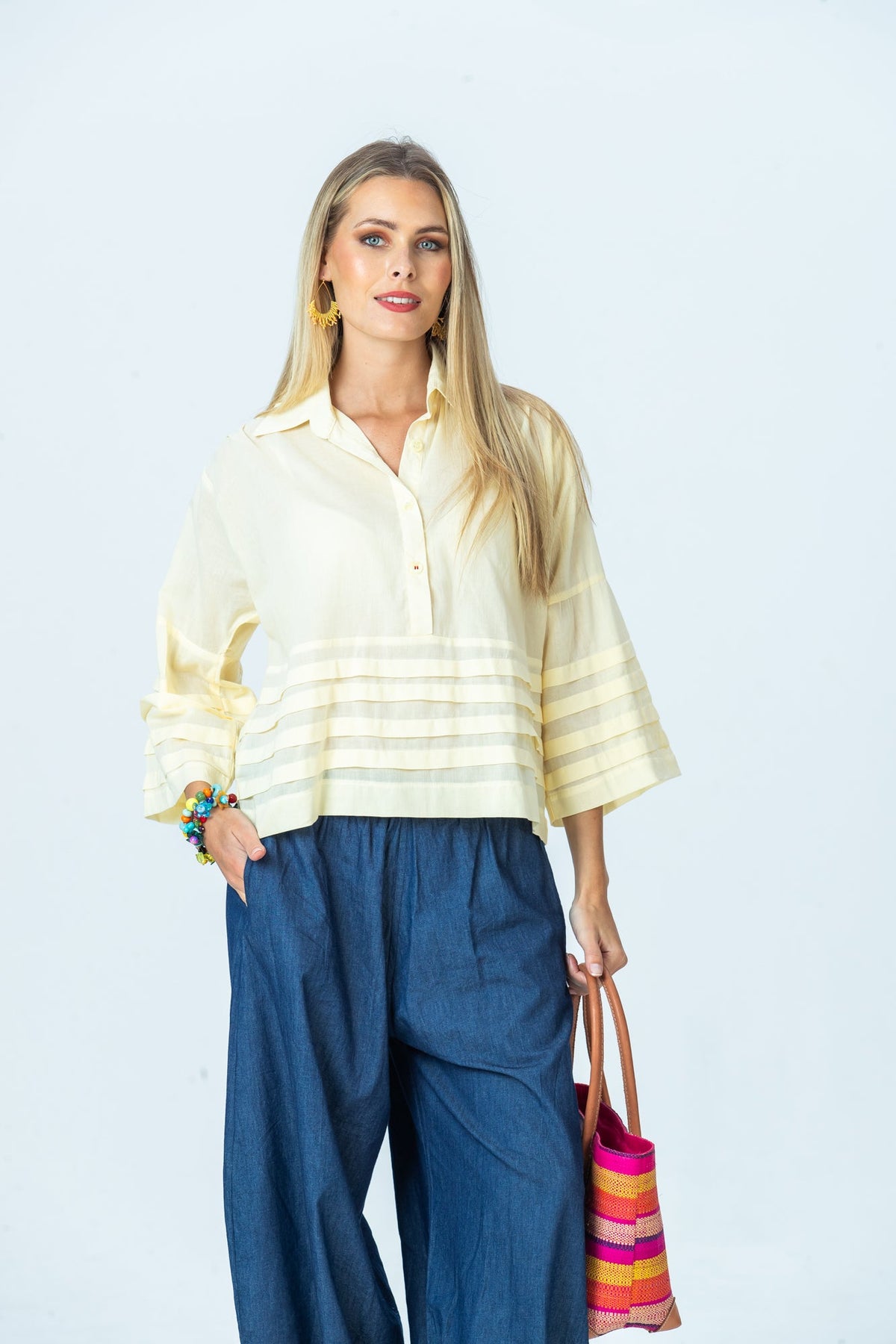 Serafina pale yellow shirt, front view with hand in pocket, carrying a woven tote