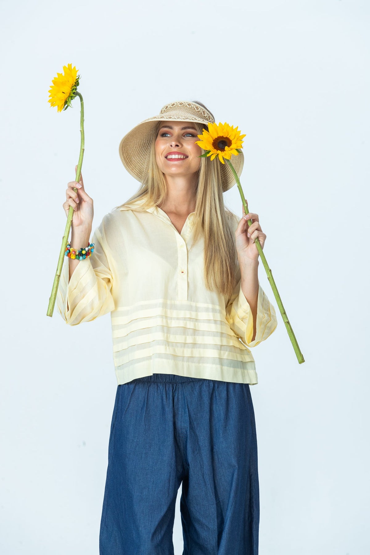 Serafina pale yellow shirt, front view in a sun visor holding sunflowers