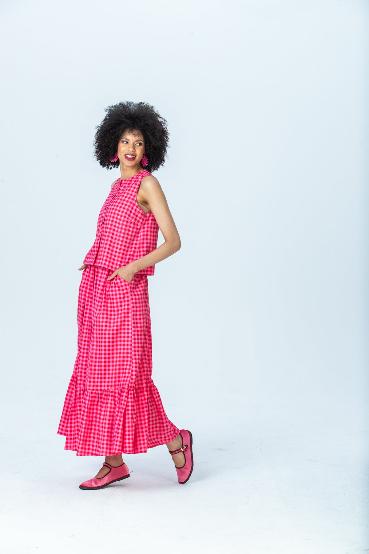 Riley red and pink check skirt, side view walking with hand in pocket
