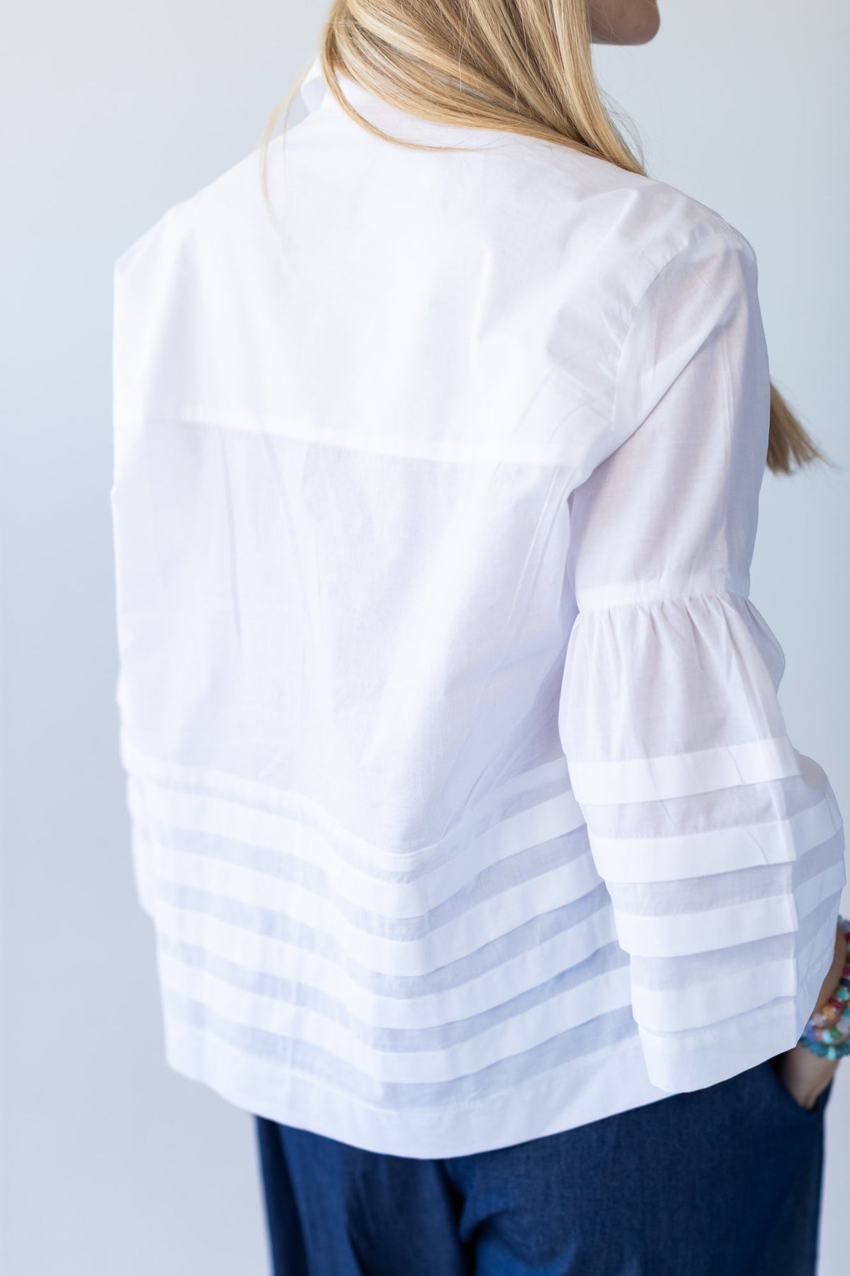 Serafina white pintuck shirt, close up of collar, placket and hem with hand at waist