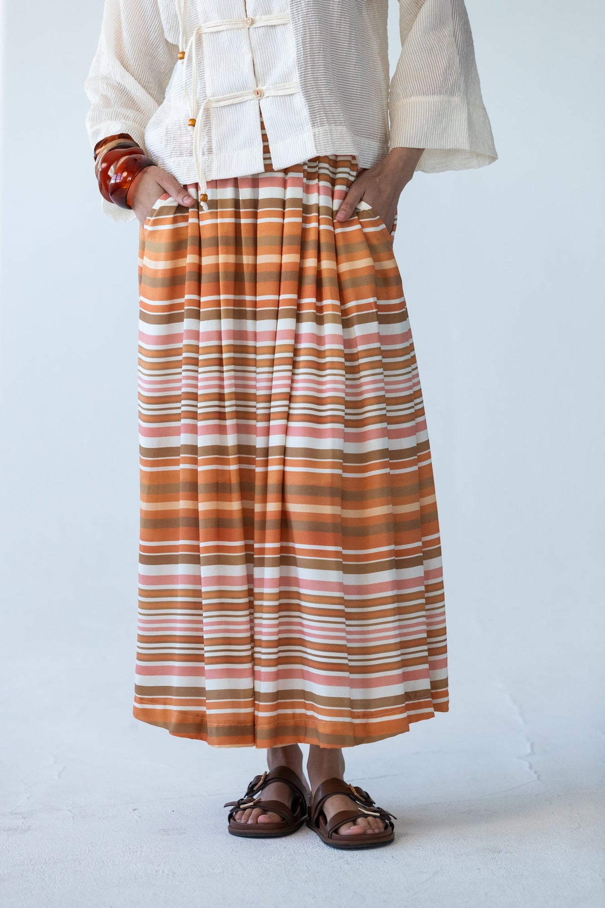 Sorrento Sunset Stripe skirt, close-up of pleated waistband, hands in pockets